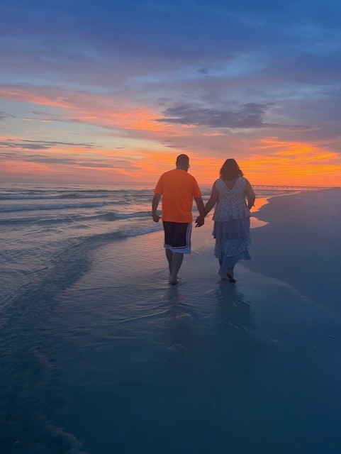 Krystal and Joe holding hands while walking along the Gulf at sunset
